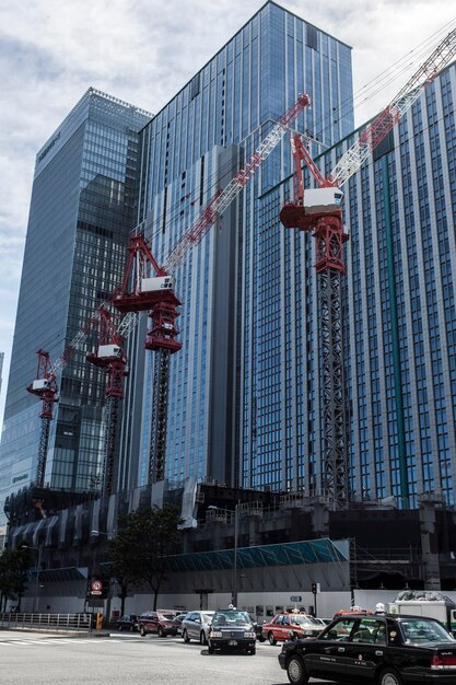 A photograph of a modern office building with several construction cranes in the background, symbolizing business expansion and investment. The sky is somewhat cloudy, reflecting uncertainty in the market.