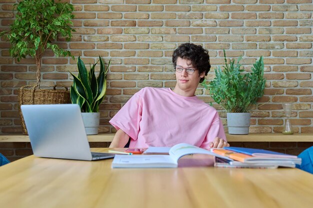 A student sitting at a desk, surrounded by textbooks, with a laptop open to a textbook rental website. The student is smiling and appears relaxed.