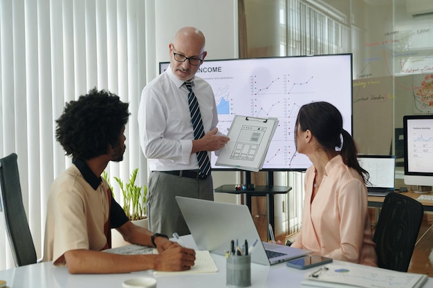 A diverse group of people in a meeting, discussing financial charts and strategies on a whiteboard, symbolizing wealth management and financial planning.